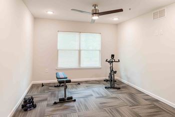 A room with a ceiling fan, a window, and exercise equipment.